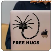Pegatina negra de criatura alienígena «FREE HUGS» aplicada en un portátil.