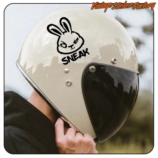 Detalle de casco de moto color crema con adhesivo SNEAK y visera oscura